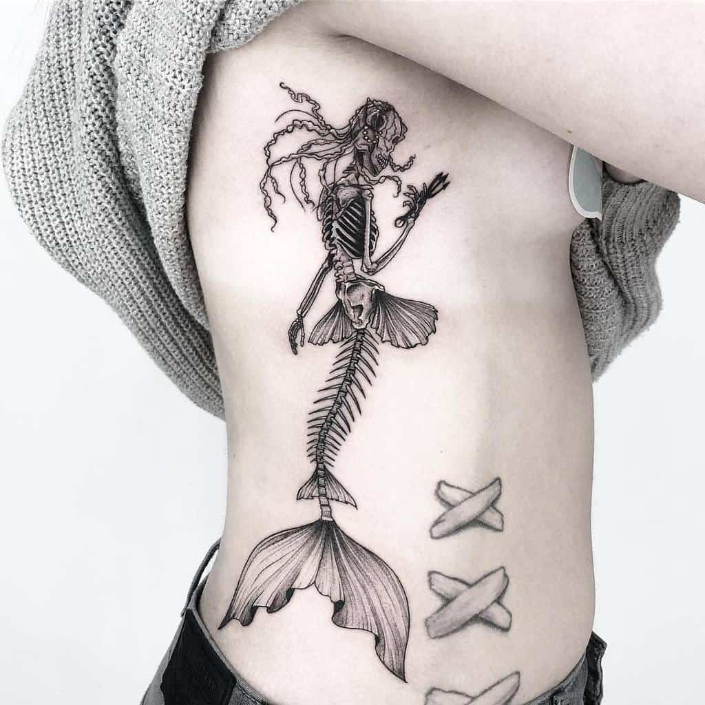 Intricate blackwork tattoo of a skeletal mermaid, featuring detailed bone structure and flowing hair, creating an eerie yet elegant design