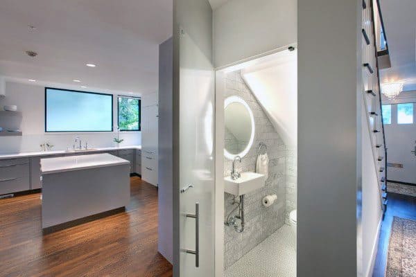 Modern half bath with circular mirror, compact sink, and toilet next to a spacious kitchen area with island