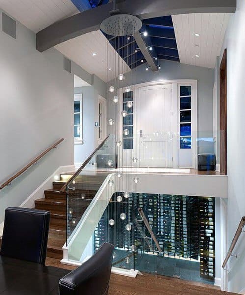 Modern staircase with glass railing, leading to a wine cellar below, featuring sleek wood flooring and sophisticated lighting