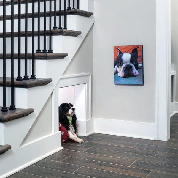 Cozy dog house tucked under the stairs, with a dog resting inside, featuring a small opening and a pet portrait hanging on the wall nearby