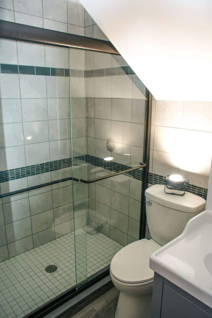Small bathroom with tiled shower under the stairs and glass sliding door.