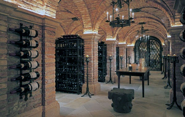A wine cellar with brick arches, racks of fine wine bottles, and a wooden table illuminated by chandeliers