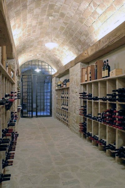 A stone wine cellar with an arched ceiling, showcasing shelves filled with wine bottles on both sides
