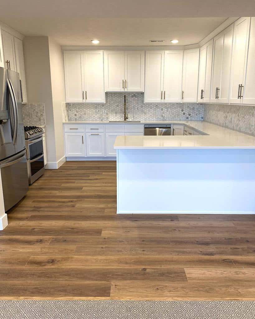 Spacious white kitchen with wooden floorboards and stainless steel appliances.