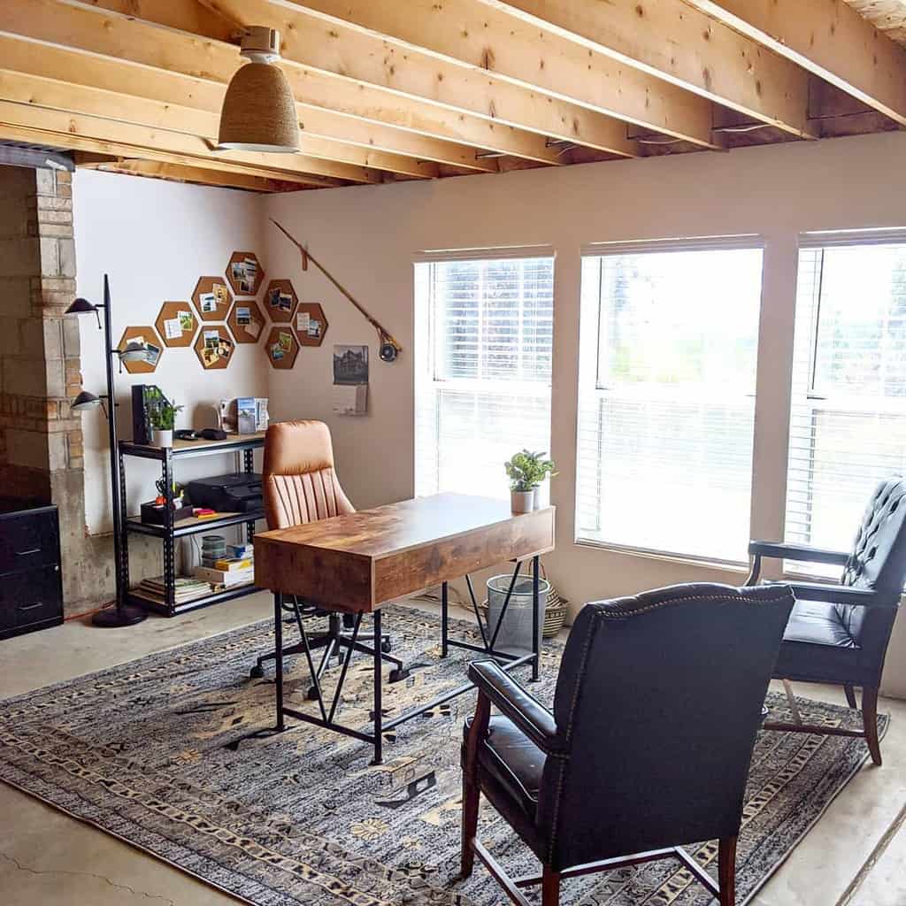 Home office with exposed wooden beam ceiling, rustic desk, and large windows.