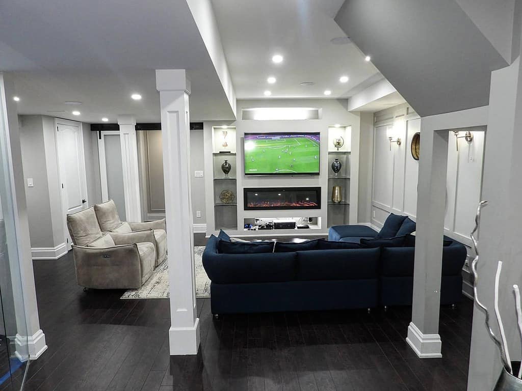 Modern living room with blue sectional couch, white paneled walls, fireplace, and mounted TV.