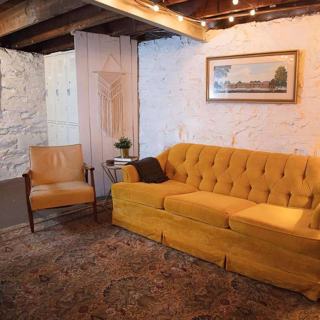 Rustic living room with mustard yellow couch, exposed beams, and textured white stone walls.