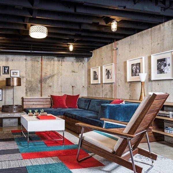 Modern basement with exposed ceiling, vintage caged light bulbs, and colorful seating area.