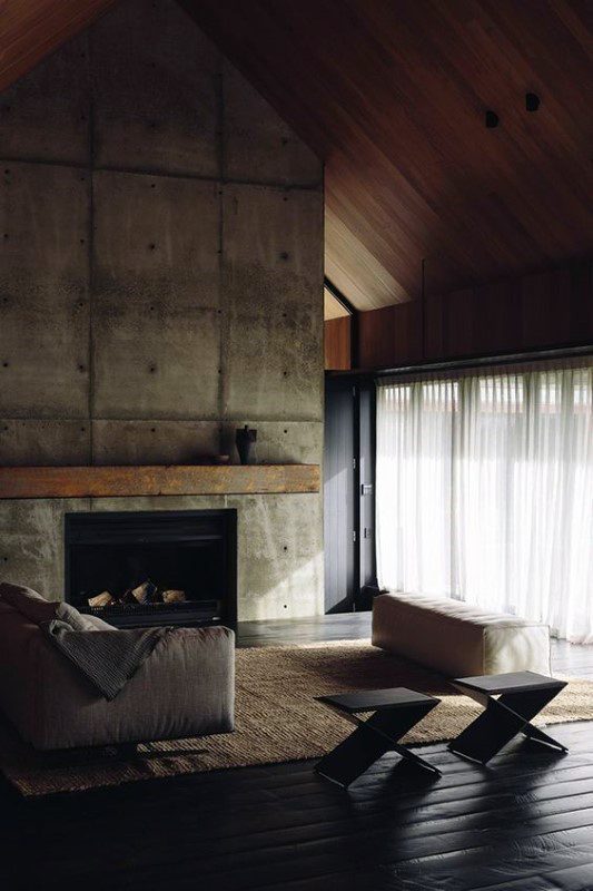 Unfinished concrete fireplace with a rustic wooden mantel, complementing the vaulted wooden ceiling.