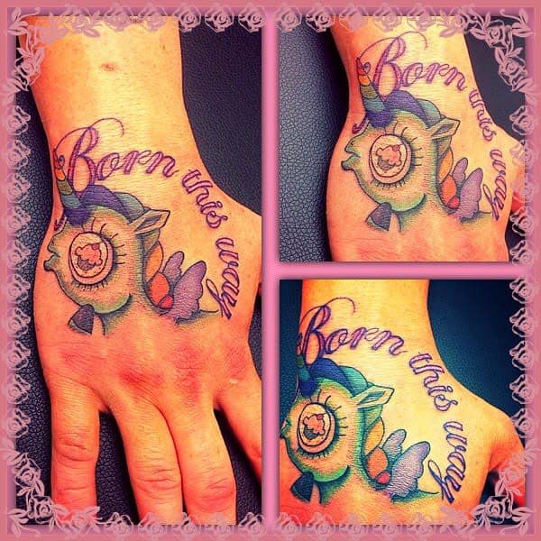 Colorful hand tattoo with a unicorn and the phrase "Born this way," framed in a pink decorative border