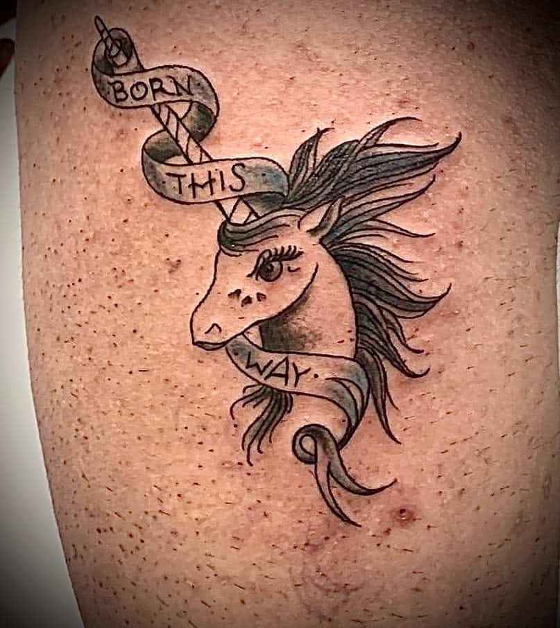 Tattoo of a unicorn's head with a flowing mane and a banner that reads "Born This Way"