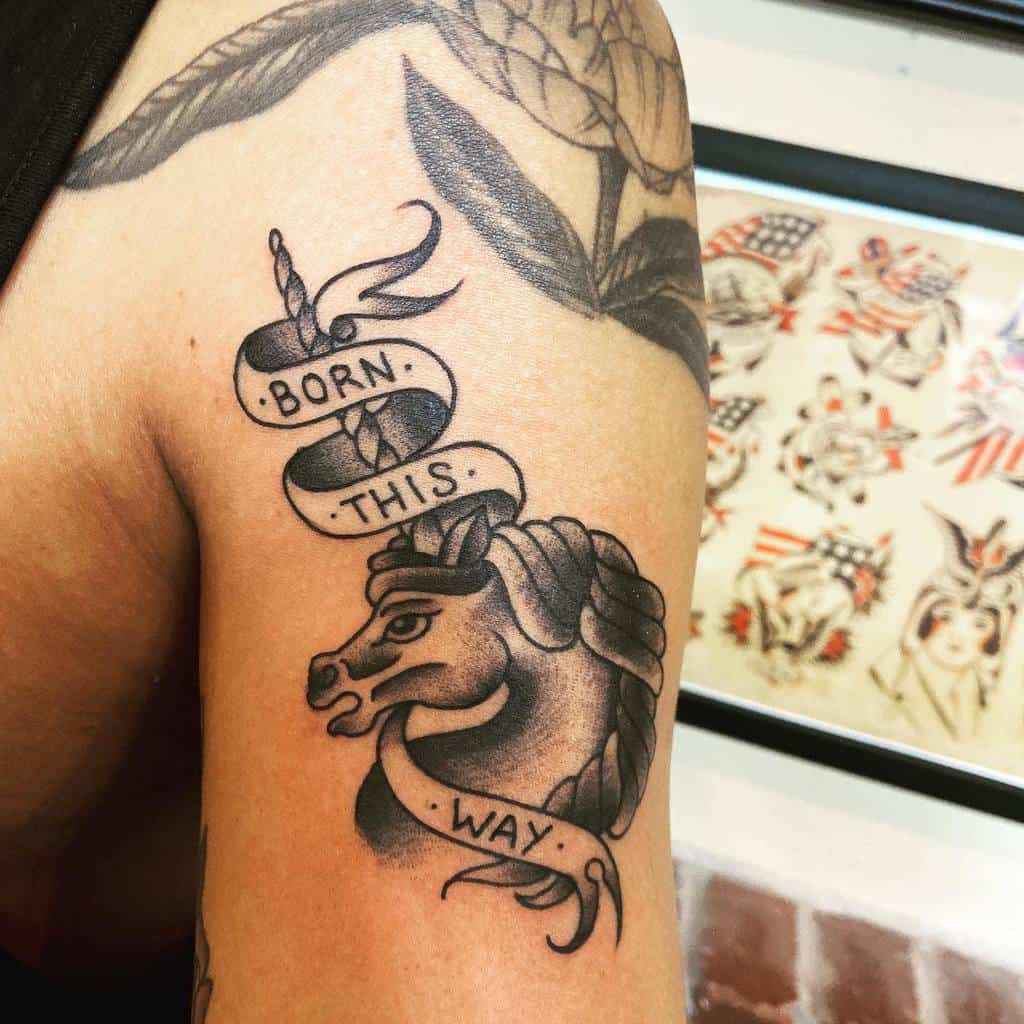 Tattoo of a unicorn with a ribbon saying "Born This Way" on an arm