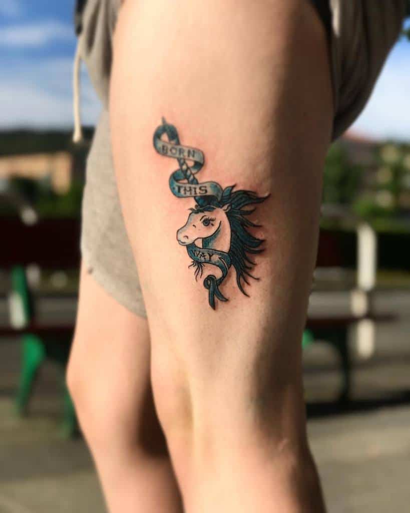 Thigh tattoo of a unicorn with a ribbon that reads "Born This Way" on a leg