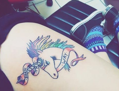 Colorful unicorn tattoo with "Born This Way" banner on a thigh