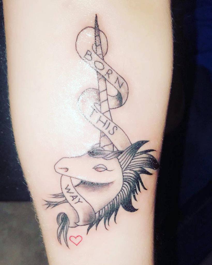 A unicorn tattoo with a banner reading "Born This Way" wrapped around the horn