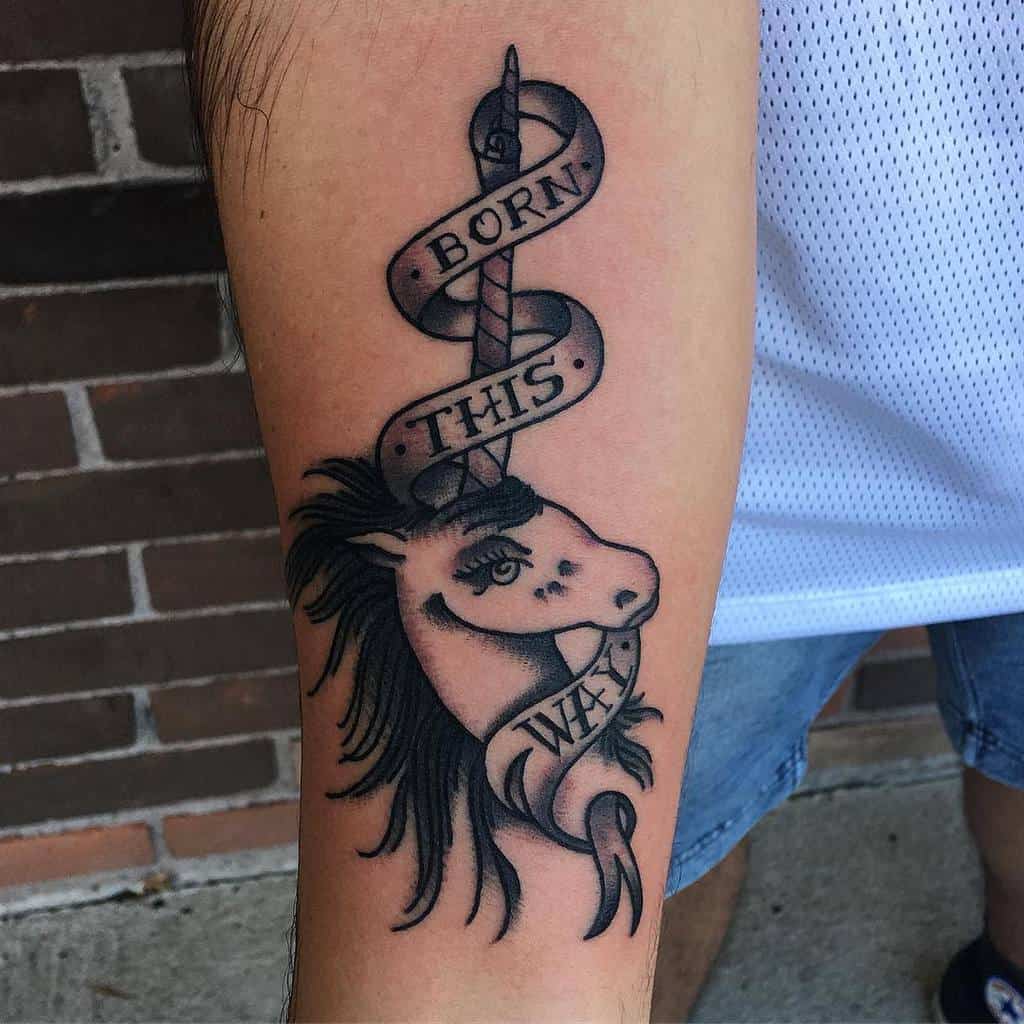 Arm tattoo of a unicorn with a banner reading "BORN THIS WAY" wrapped around the horn