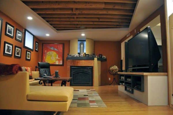 Cozy basement with exposed wooden beams, fireplace, and warm-toned decor.