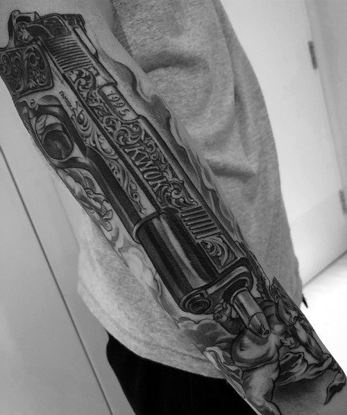 Realistic black and gray full-sleeve tattoo of an intricately engraved 1911 pistol, designed with detailed shading and artistic embellishments.