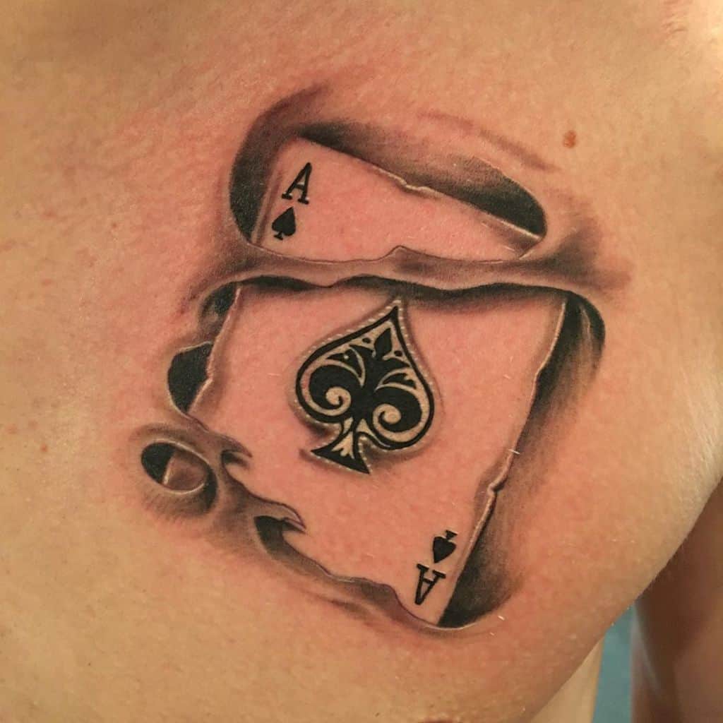 A black-and-white tattoo featuring the Ace of Spades card, with a torn effect revealing the design