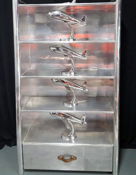 Silver shelf with four airplane models on separate shelves and a drawer at the bottom