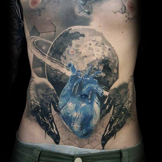 Surreal torso tattoo of a blue anatomical heart with Saturn-like rings, placed in front of a moon and flanked by abstract figures.