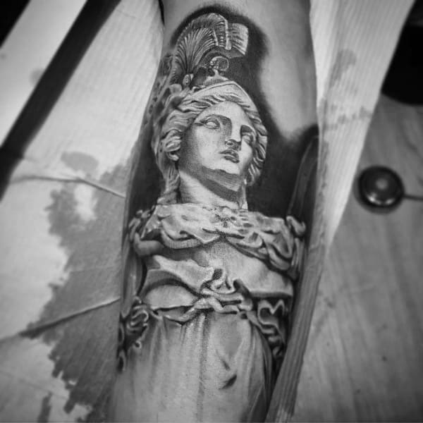 Realistic Athena tattoo resembling a marble statue with intricate drapery, crested helmet, and soft black and grey shading on forearm