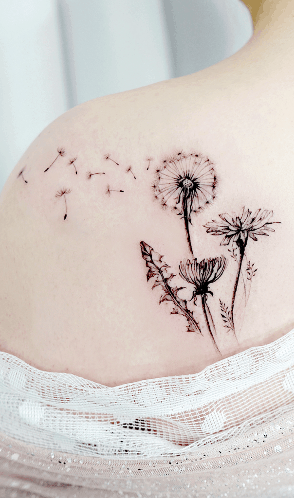 This tattoo features detailed dandelions and wildflowers with seeds floating away, symbolizing freedom and movement across the shoulder. The design is both delicate and striking.