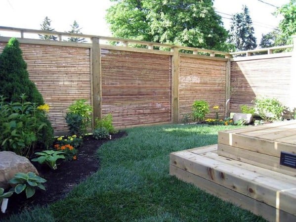 Bamboo privacy fence with wooden frame in a landscaped backyard with raised deck and plants.
