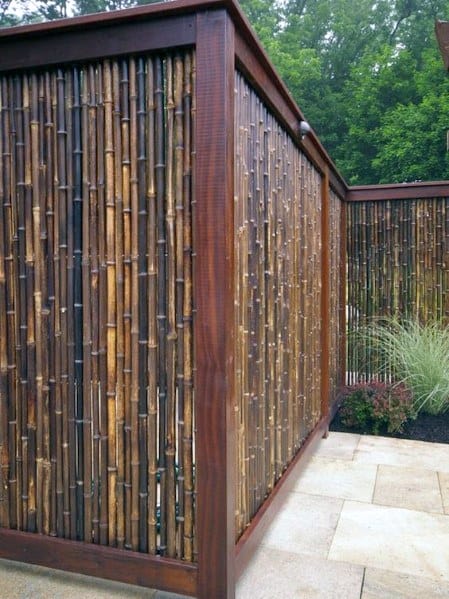 Dark bamboo fence with a wooden frame surrounding a modern patio in a garden setting.