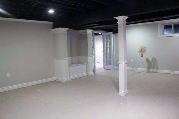 Basement with black exposed ceiling, white columns, and neutral painted walls.