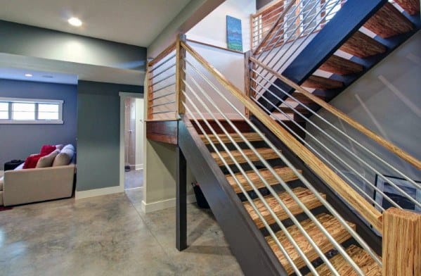 Modern wooden staircase with horizontal metal handrails and polished concrete floors in basement.