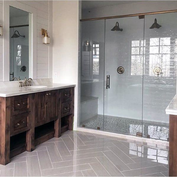 Large glass-enclosed shower with brown wood vanity and herringbone tile floor.