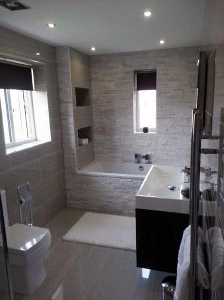 Bathroom with natural stone brick tiles, built-in bathtub, and recessed shelving.