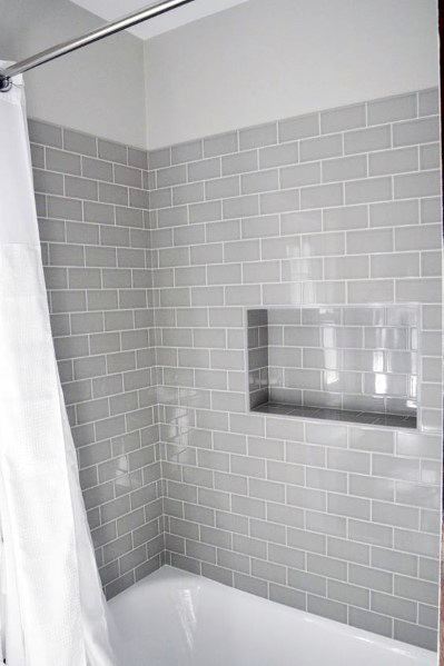 Light gray beveled subway tile shower wall with built-in shelf above white bathtub.