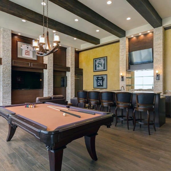 Luxurious billiard room with exposed beams, yellow accent walls, and a built-in bar area.