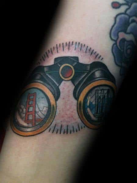 Colorful binoculars tattoo featuring reflections of iconic bridges, symbolizing travel, exploration, and a love for cityscapes.
