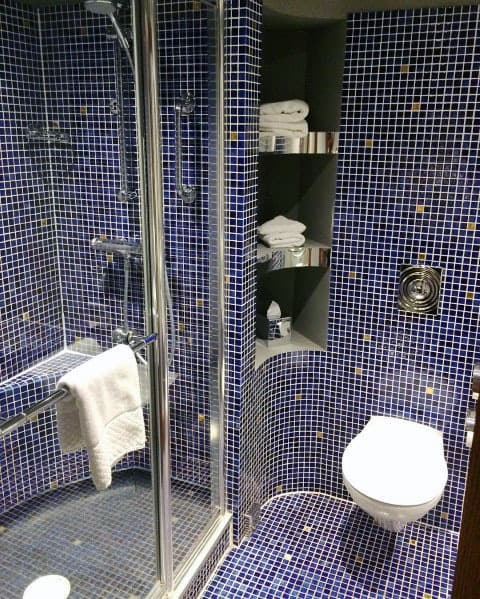 Bathroom with blue mosaic tiles, glass shower enclosure, built-in shelves, and wall-mounted toilet.
