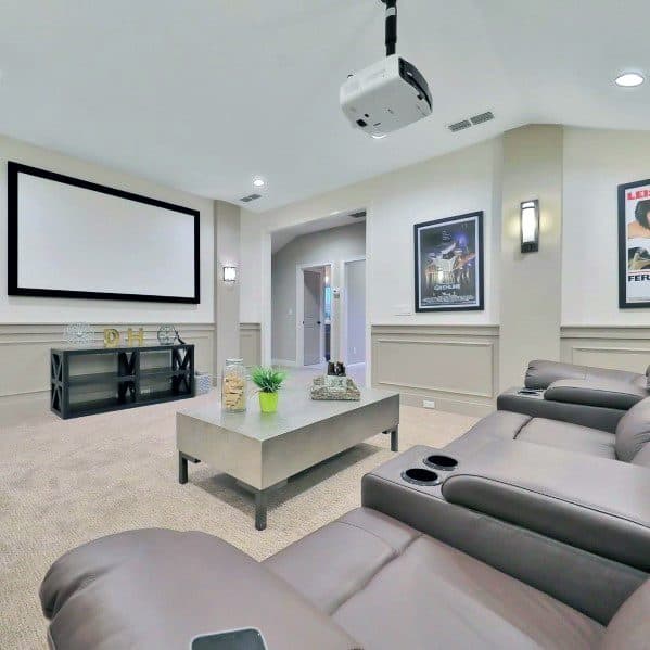 Home theater with leather recliners, projector, framed posters, and minimalist coffee table.
