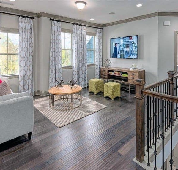 Bright sitting area with hardwood floors, patterned curtains, round coffee table, and colorful stools.