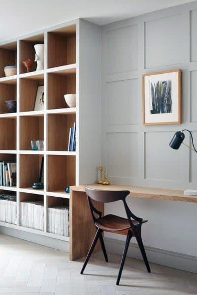Minimalist home office with a wooden desk, dark chair, bookshelves, and abstract wall art