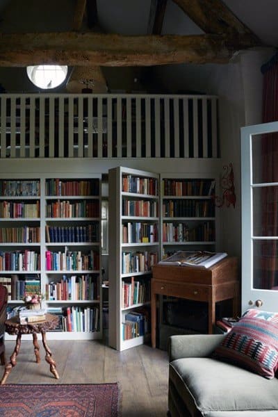 Cozy library with a loft, bookshelf, armchair, and a wooden desk under a beamed ceiling
