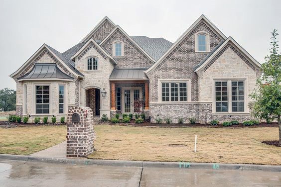 Spacious home with light stone and brick cladding, gabled rooflines, metal awnings, and a covered porch for an inviting curb appeal