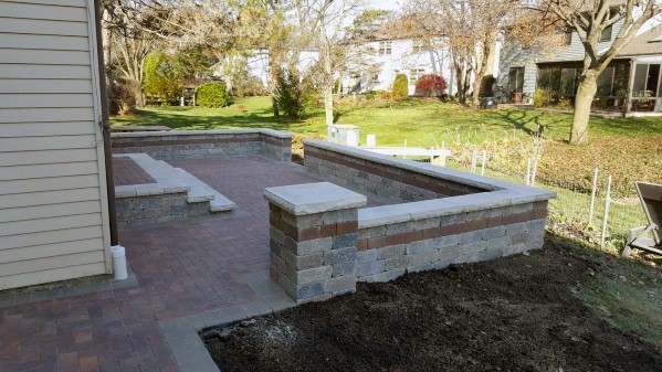 Brick patio with retaining walls and steps, nestled by a house, overlooks a grassy backyard