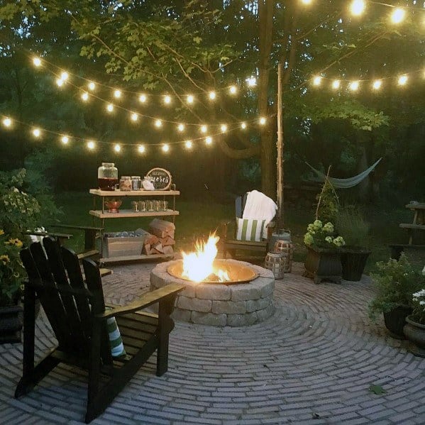 Cozy outdoor patio with brick fire pit, chairs, string lights, and a hammock in the background