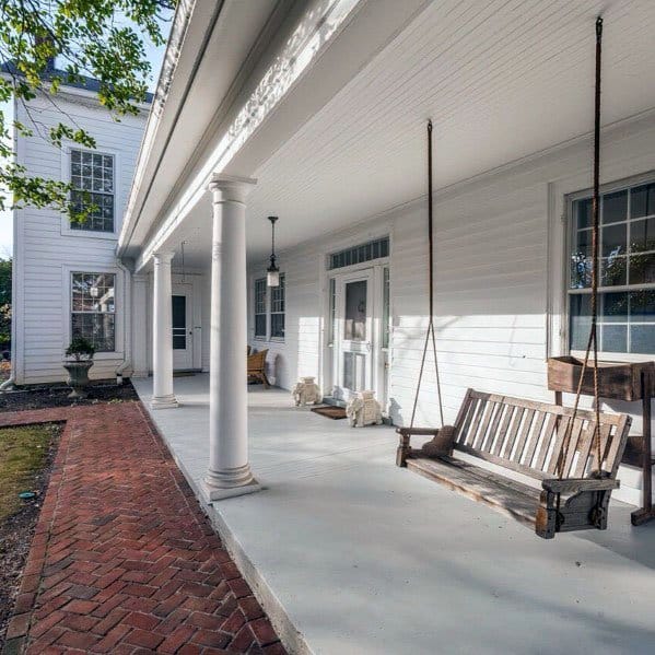 White house porch with a wooden swing and brick walkway