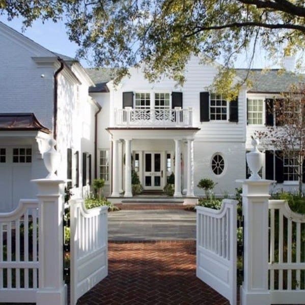 White colonial-style house with black shutters and a brick walkway through an open gate