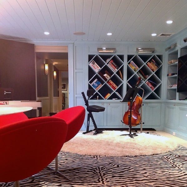 Creative multipurpose room with a unique built-in bookcase featuring diagonal shelves, light blue cabinetry, bold red chairs, and a zebra-print rug, perfect for music practice and leisure
