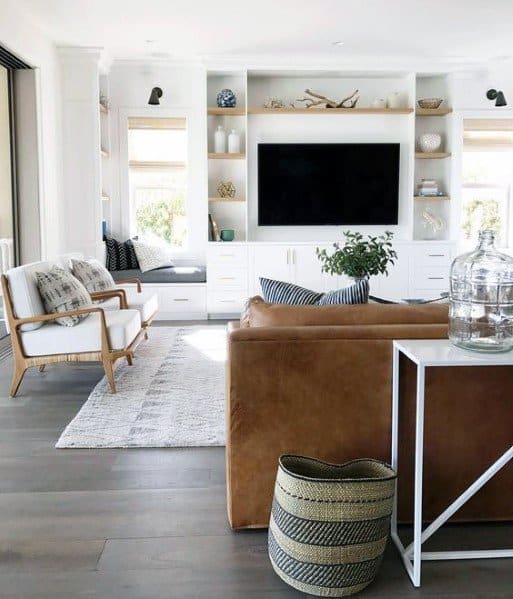 Bright living room with a built-in bookcase and entertainment center, featuring white cabinetry, open shelving with decorative items, a cozy window seat, and modern furniture for a welcoming ambiance