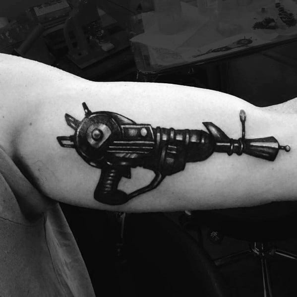 Bold black and grey Call of Duty Ray Gun tattoo on the bicep, featuring detailed shading and a realistic design of the iconic zombie weapon.