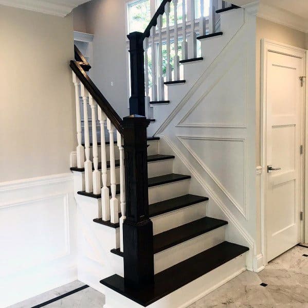 Wooden staircase with white paneling, chair rail detailing, and a black railing in a modern home interior